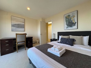 A hotel room with a bed, a desk, a chair, a painting, and a door.