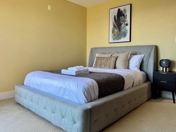 A bedroom with a bed, pillows, a bedside table, and a wall art piece.