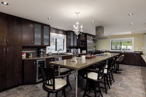 A modern kitchen with dark wood cabinets, a central island with bar stools, stainless steel appliances, and a chandelier.