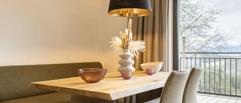 A modern dining area with a wooden table, a black lamp, and a view of a balcony.