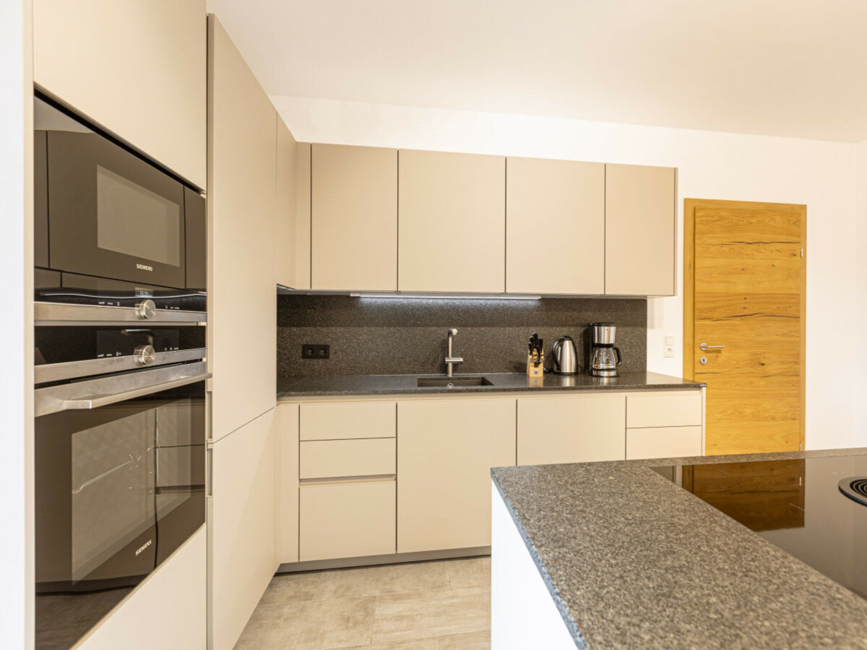 Een moderne keuken met ingebouwde apparatuur, een granieten aanrechtblad en lichtkleurige kastjes.