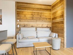 A modern living room with a wooden accent wall, a sofa, a coffee table, and a small stool. - Apartment With 1 Bedroom (Sankt Martin am Tennengebirge)