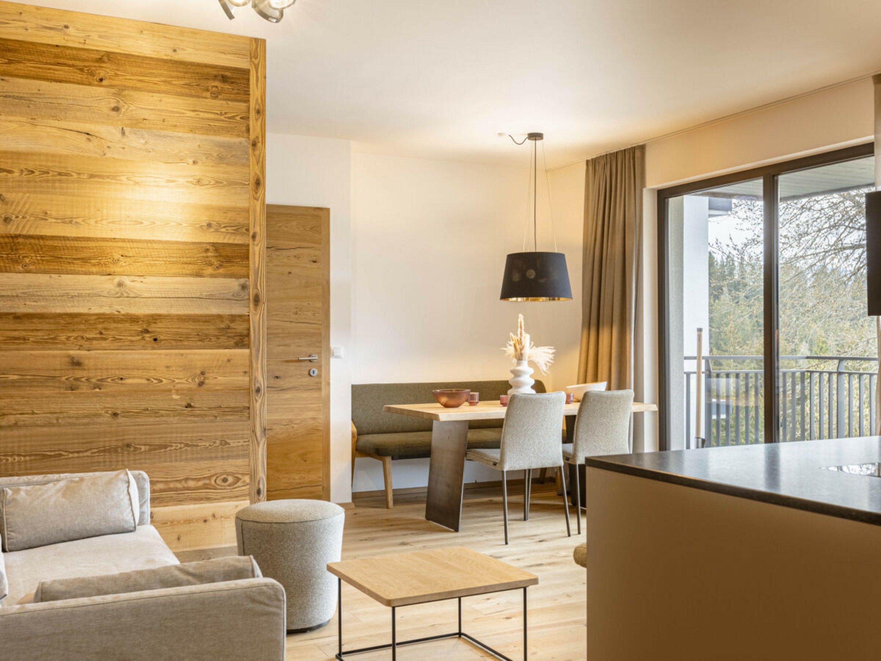 Una sala de estar moderna con una pared de acento de madera, un comedor con mesa y sillas, y un ventanal con vistas a árboles.