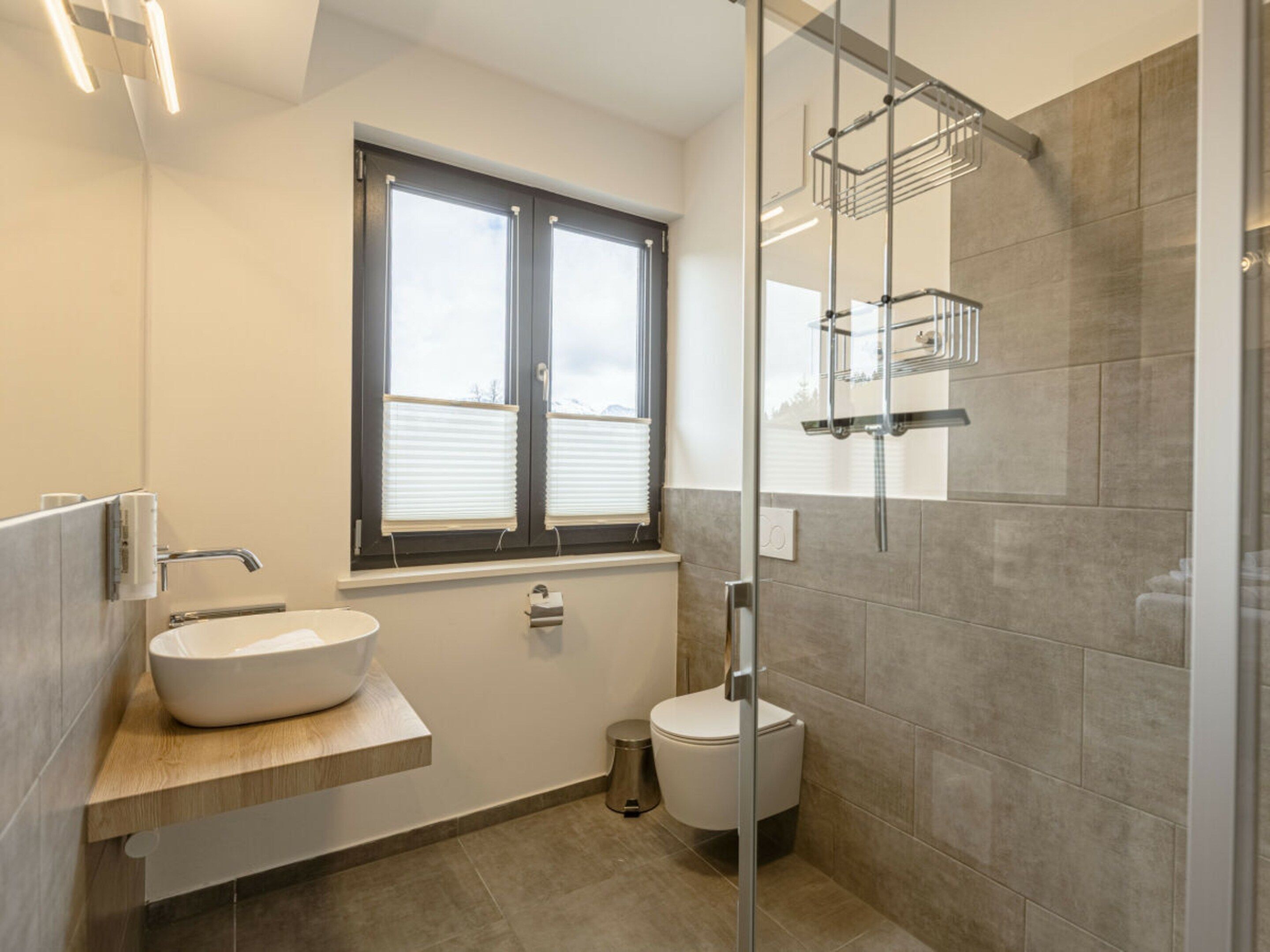 A modern bathroom with a large window, a sink, a toilet, and a shower area.