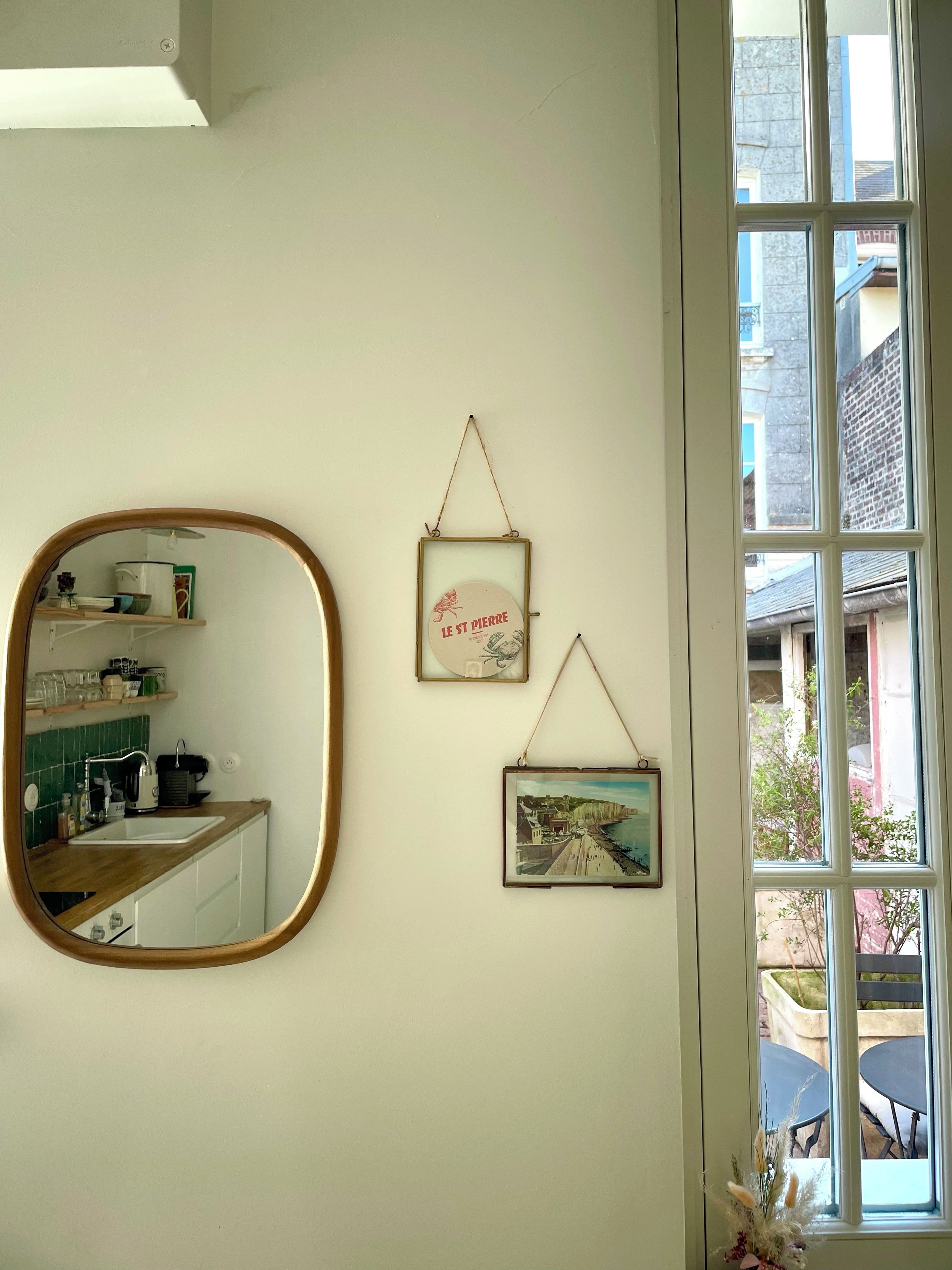 A kitchen with a large mirror, a framed picture, and a window with a view of the outside.