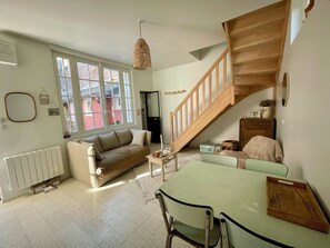 A cozy living room with a sofa, a dining table with chairs, a staircase, and a large window. - L'Annexe : maison cosy avec jardin et vue mer (Ault)