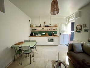 Cuina compacta amb zona de menjador, un sofà i un llum penjant.