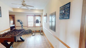 A room with a foosball table, exercise equipment, a ceiling fan, and a motivational wall art. - Oceanfront 4x4 retreat w/ Private Pool, Hot Tub, Elevator & Sauna – Sleeps 22 (Corolla)