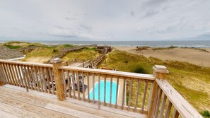 Eine Holzterrasse mit Pool, Strand und einer Promenade, die zum Strand führt.