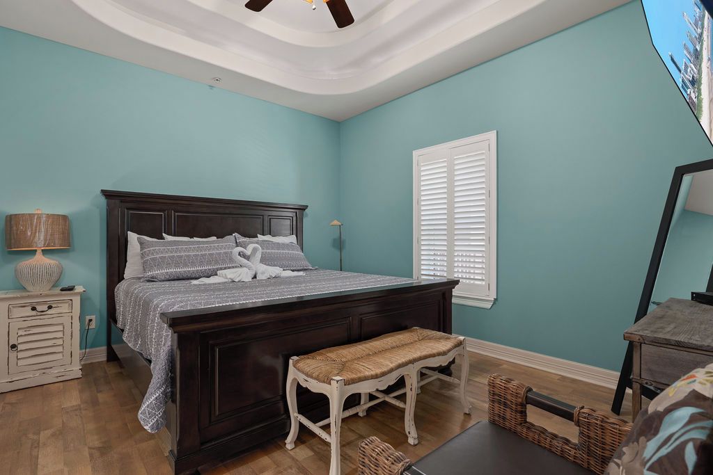 A bedroom with a dark wooden bed, a white bench, a lamp, and a window with blinds.