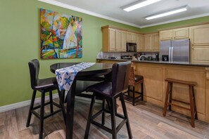 A kitchen with wooden cabinets, a stainless steel refrigerator, and a dining area with a table and chairs. - Fabulous Bayside Condo from Rent On Padre (South Padre Island)