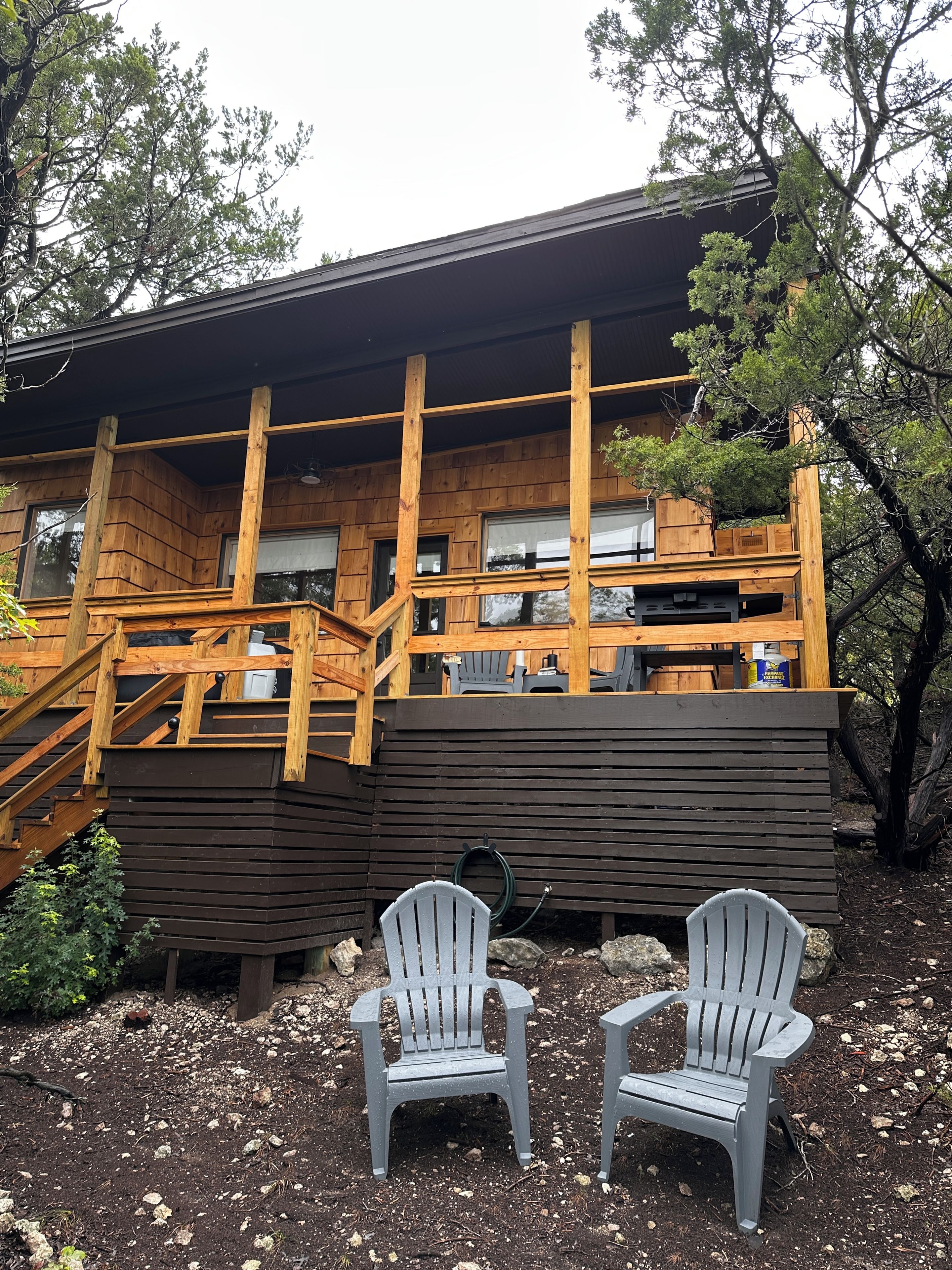 Una baita di legno con un balcone, due poltrone Adirondack e un giardino.