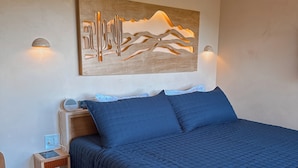 Quarto com cama, mesa de cabeceira, obra de arte na parede e criado-mudo.