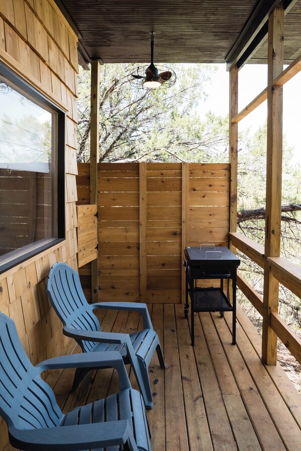 A covered outdoor seating area with wooden walls, a table, and two chairs.
