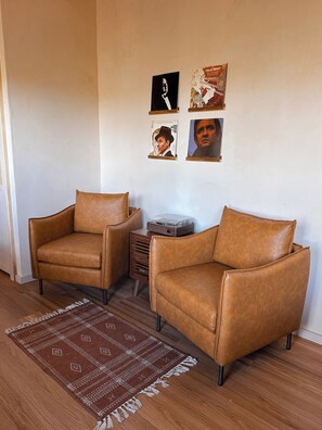 A room with two brown leather armchairs, a small wooden side table with a record player, and a patterned rug on a wooden floor.