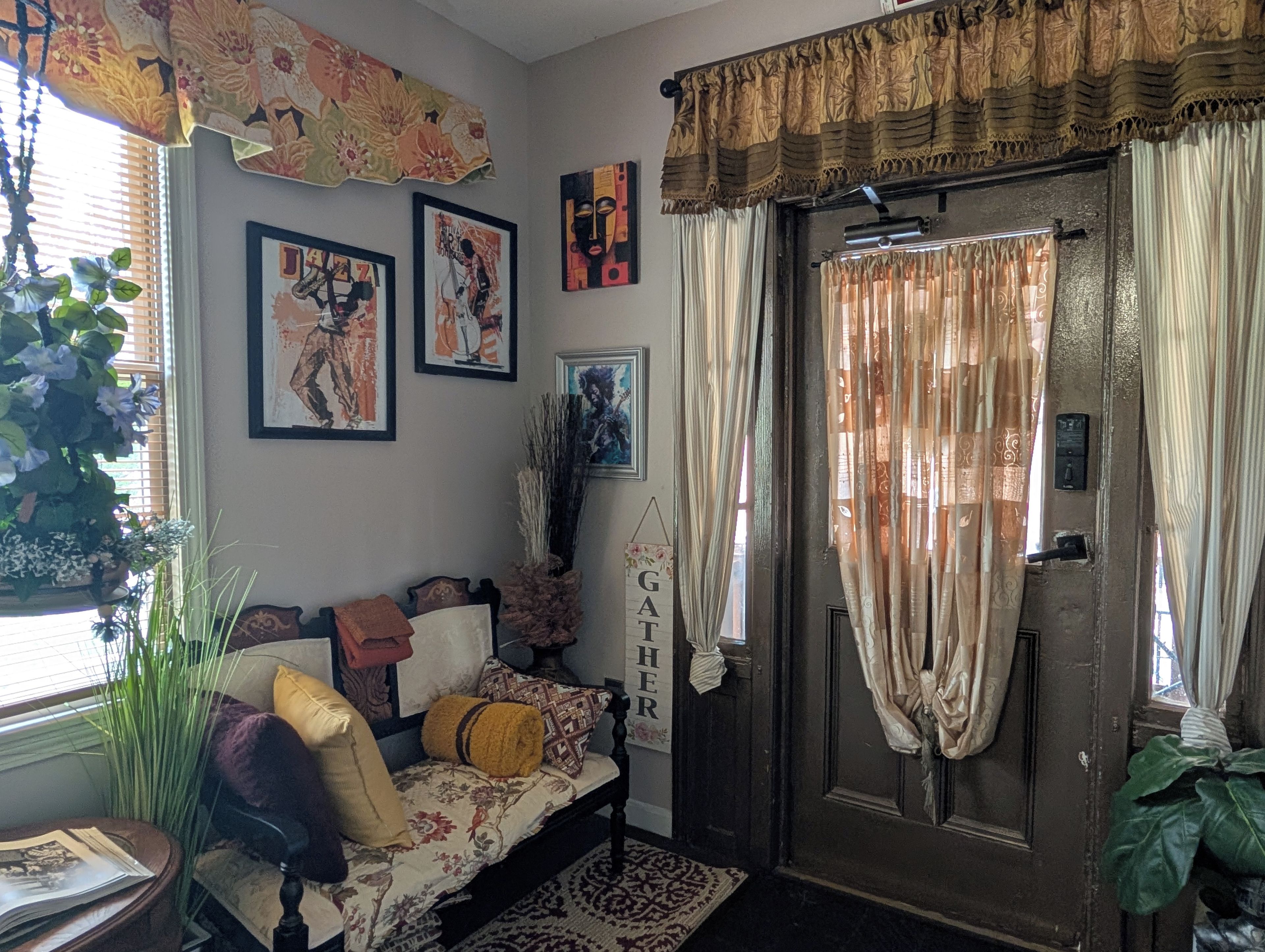 A cozy living room with a sofa, decorative pillows, wall art, and a door with curtains.