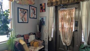 A cozy living room with a sofa, decorative pillows, wall art, and a door with curtains.