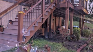 A wooden house with a staircase leading to a porch, surrounded by a garden with various plants.