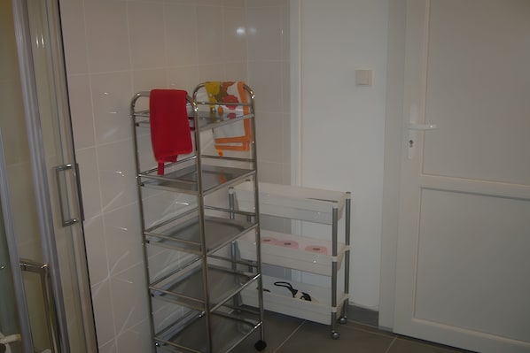 A bathroom with a metal shelf unit holding towels and a toilet paper holder.