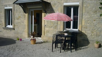 A stone building with a door, a window, and a table with chairs outside.