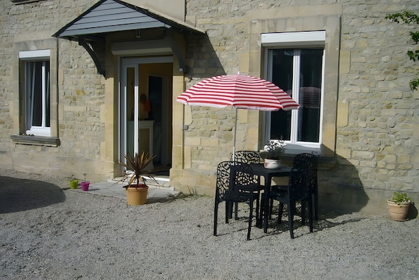 A stone building with a door, a window, and a table with chairs outside.