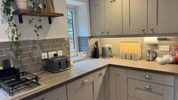 A modern kitchen with grey cabinets, a wooden shelf with a potted plant, a toaster, a coffee maker, and a kettle on the counter.