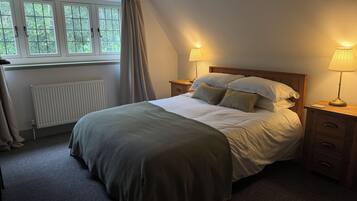 A bedroom with a bed, two bedside tables, a window with curtains, a radiator, and a lamp on each bedside table.