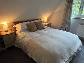 Ein ordentlich bezogenes Bett mit weißer Daunendecke und zwei Kissen, flankiert von Nachttischen mit Lampen, in einem Zimmer mit schrägem Dach.