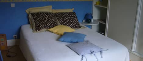 Ein Bett mit mehreren Kissen, ein Nachttisch mit Lampe und eine Steckdose an der Wand.