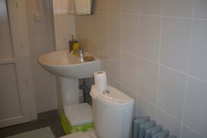 Ett badrum med ett vitt handfat, en toalett och en grön pall.