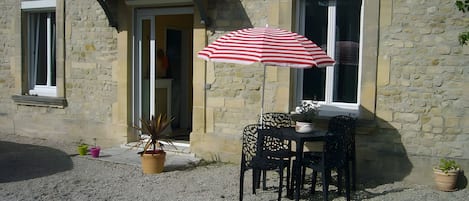 A stone building with a door, a window, and a table with chairs outside.