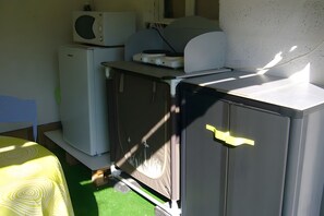 Cocina compacta con refrigerador, microondas y una pequeña encimera con un microondas encima.