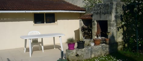 Un patio con una mesa y silla blancos, rodeado de macetas con plantas y un muro de piedra.