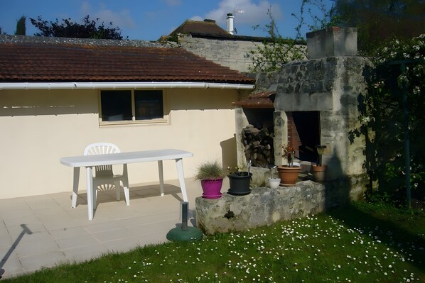 Un patio con una mesa y silla blancos, rodeado de macetas con plantas y un muro de piedra.