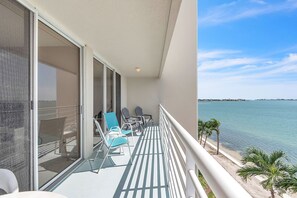 A balcony with a view of the sea, equipped with chairs and a table.