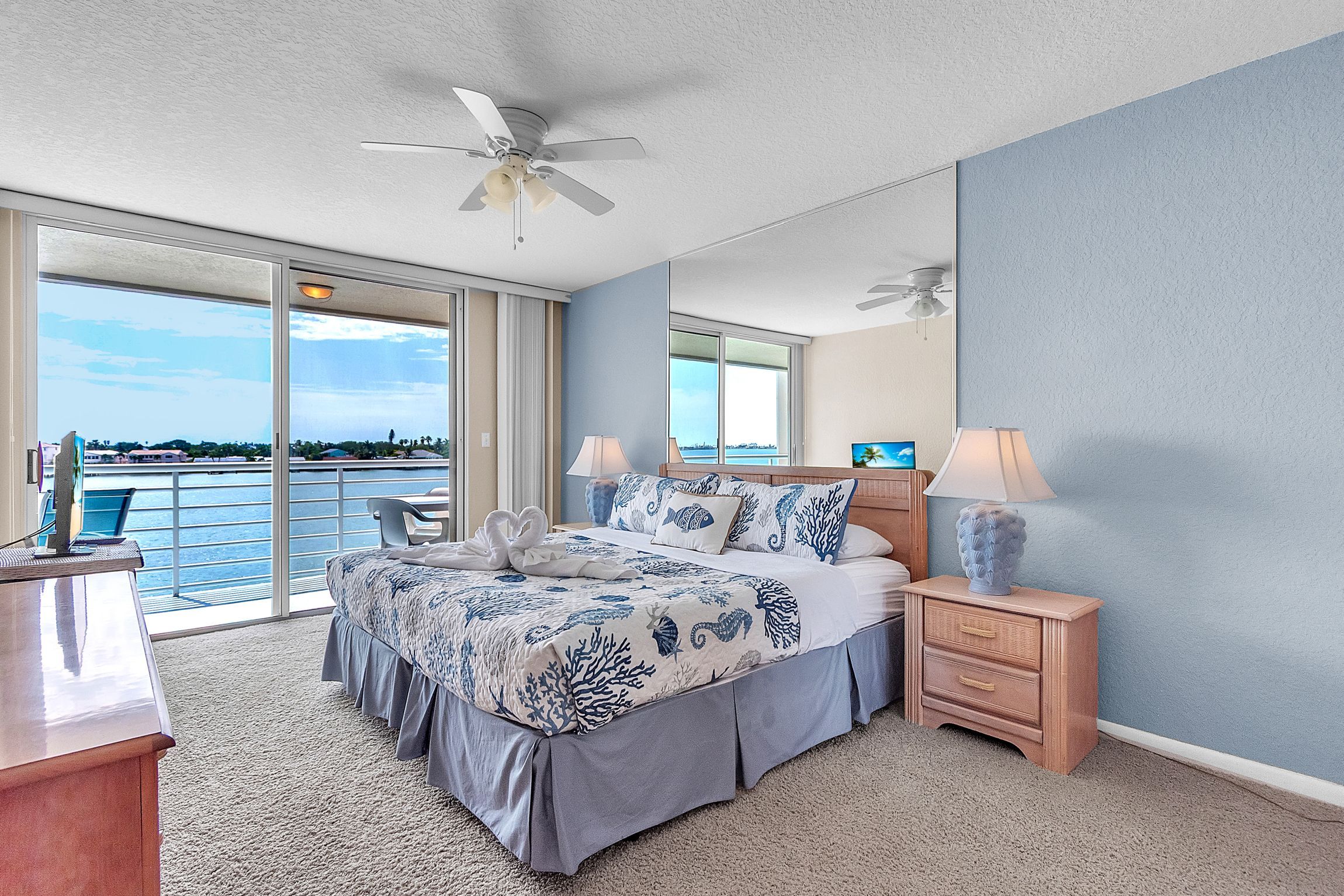 A hotel room with a bed, two bedside tables, a desk, a chair, a large window, and a ceiling fan.