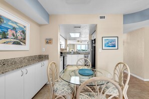 A dining area with a glass table surrounded by chairs, a kitchen in the background, and artwork on the walls. - Resort Style Amenities + Quick Drive to Beach | Bahia Vista 478 (Saint Petersburg)