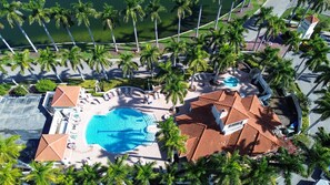 An aerial view of a resort with a central swimming pool, palm trees, and a small tower structure. - Resort Style Amenities + Quick Drive to Beach | Bahia Vista 478 (Saint Petersburg)