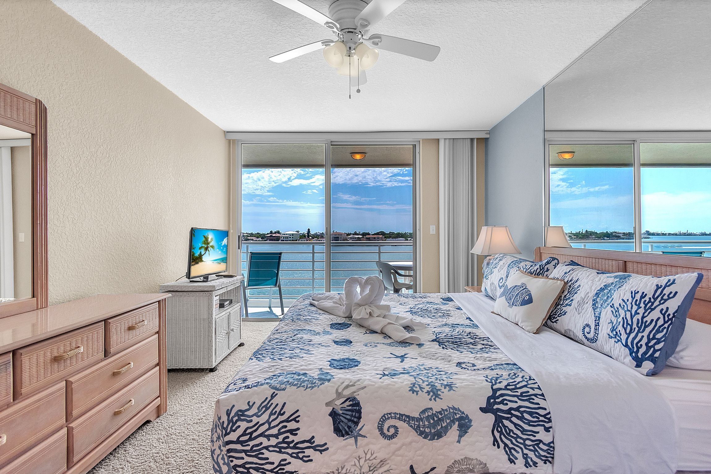 A hotel room with a bed, a dresser, a television, and a balcony with a view of the sea.