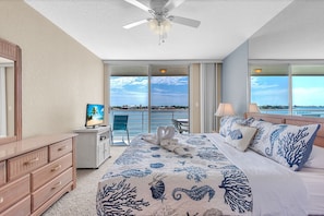 A hotel room with a bed, a dresser, a television, and a balcony with a view of the sea.