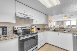 A modern kitchen with white cabinets, a stove, a microwave, and a ceiling fan. - Resort Style Amenities + Quick Drive to Beach | Bahia Vista 478 (Saint Petersburg)