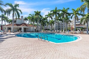 A swimming pool with a brick deck, surrounded by palm trees and a building with a red-tiled roof. - Resort Style Amenities + Quick Drive to Beach | Bahia Vista 478 (Saint Petersburg)