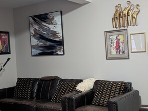 A living room with a dark brown leather sofa, a large abstract painting, and a wall-mounted sculpture of golden animal figures. - 146-4 Miles Davis, Jazz Great! A place 2 Rest & Relax.  	1 Bedroom Studio. (New London)