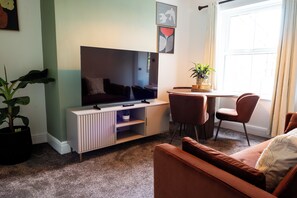 Ein Wohnzimmer mit Flachbildfernseher, einer Couch, einem Couchtisch und einer Topfpflanze.