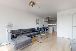 Una sala moderna con un sofá modular, una mesa de centro de vidrio y un comedor con sillas.