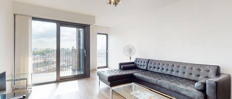 A modern living room with a sectional sofa, a glass coffee table, and a view of the city through large windows.