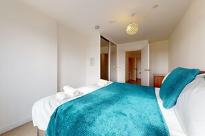 Habitación de hotel con una cama, un plaid azul, un almohadón blanco y una lámpara colgante.