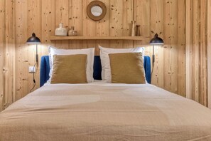 Cama com cabeceira de madeira, duas luminárias laterais e uma estante com objetos decorativos.