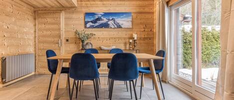 Un interior de madera con una mesa de comedor y sillas, un cuadro de una montaña y una ventana con vistas a árboles.