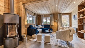 Et hyggeligt interiør i en træhytte med en brændeovn, en blå sofa, en beige lænestol og et lille bord.